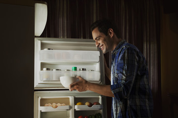 Young man standing in the kitchen searching food in the fridge at night