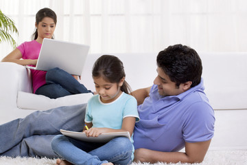 Father assisting daughter while mother using laptop in the background 