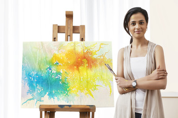 Portrait of confident female artist standing by painting 