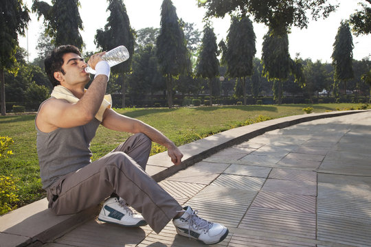 Young man with towel round shoulders drinking water after workout 