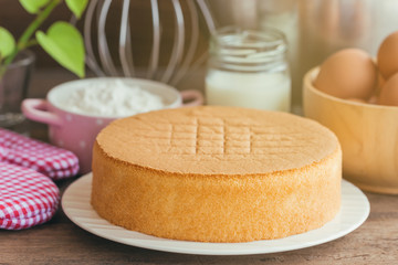 Homemade sponge cake on white plate.Soft and lite delicious sponge cake with ingredients: eggs flour milk on wood table. Homemade cake with ingredients in homemade bakery concept for bakery background