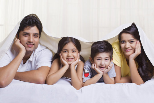 Portrait of parents with children lying under bed cover 