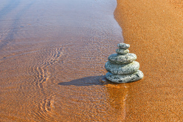 Fototapeta na wymiar Balance stone on sand coast near water 