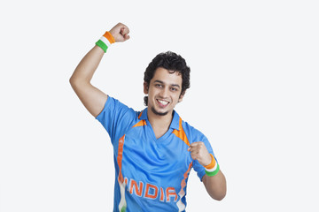 Portrait of young man in Indian cricket team jersey cheering up with clenched fists over white...