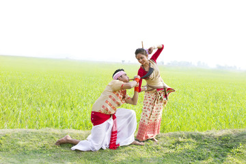 Bihu man blowing on a pepa while Bihu woman dances to his tune 