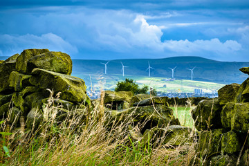  Stone wall on a farm with background bright moody blue clouds and wind turbines over hills in...