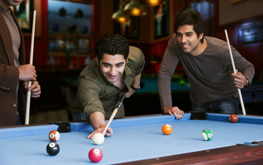 Young man aiming at cue ball while friends standing by pool table