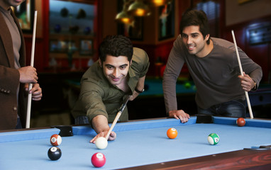 Young man aiming at cue ball while friends standing by pool table 