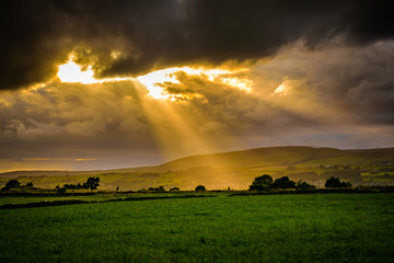 Summer sunset over landcape with sun rays through clouds