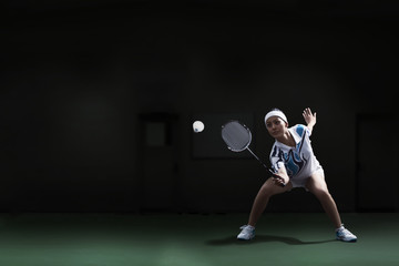 Full length of woman hitting shuttlecock with badminton racket at court - obrazy, fototapety, plakaty