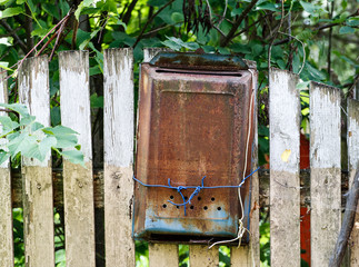Old metal rusted mail box hanged on a wooden fence under green tree