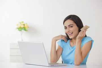 Portrait of happy young woman with credit card and laptop at home