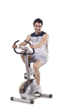 Portrait of a young fit man on exercise bike over white background 