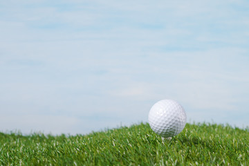 golf ball stands on a tee against the sky