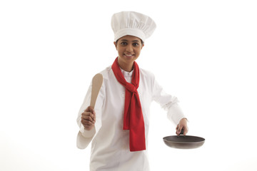 Portrait of a female chef holding frying pan and wooden spatula isolated over white background 