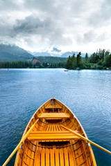 Obrazy na Szkle  Drewniana piękna łódź na jeziorze otoczonym górami.