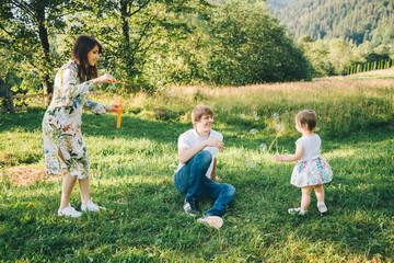 father and mother play with his daughter with soapbubble