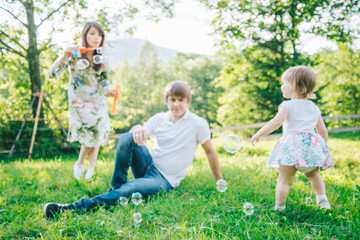 father and mother play with his daughter with soapbubble