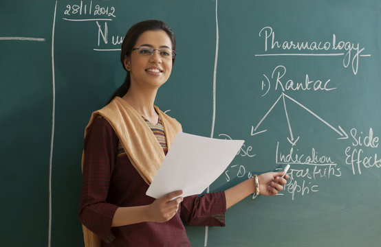 Young female teacher explaining a lesson while standing against chalkboard 