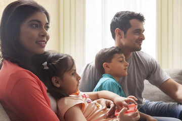 Family with son and daughter sitting on sofa and watching TV