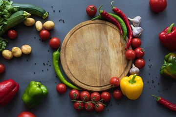 top view of fresh ripe vegetables with wooden cutting board on grey
