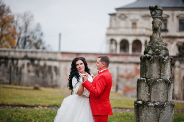 Beautiful wedding couple walking and posing next to the old fountain in the area with a lovely view of a castle on the background. Rainy weather.