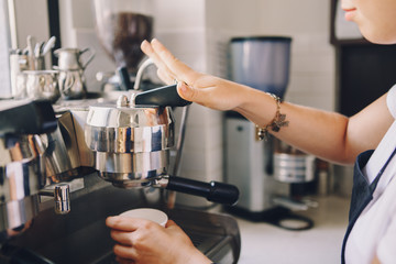 Closeup of young Caucasian barista hands holding paper cup making coffee using  coffee machine. Woman pouring coffee from professional espresso machine. Toned with film filters.