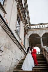 Awesome newly married couple enjoying each other's company on the stairs of old castle on a rainy wedding day.