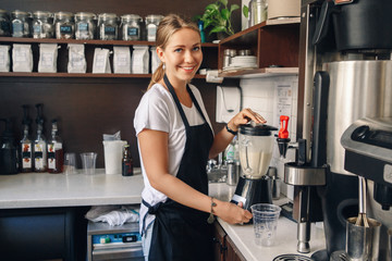 Portrait of  happy beautiful young Caucasian smiling woman barista preparing smoothie with ice....