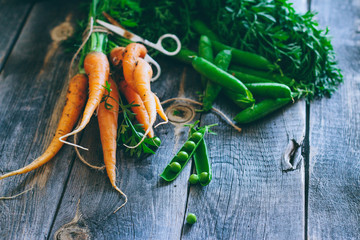 Fresh carrots with green tops and pods of peas on a wooden background, harvest, autumn