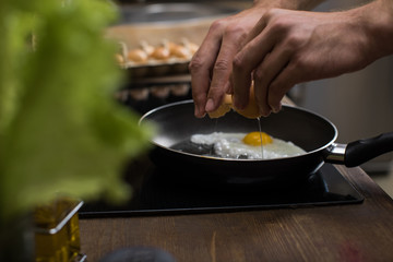 partial view of young man preparing eggs for breakfast in kitchen at home