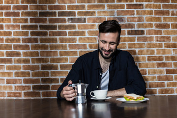 handsome bearded young man drinking coffee and eating sandwich at morning
