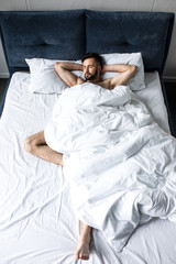 handsome shirtless bearded man sleeping in bed under white blanket in bed