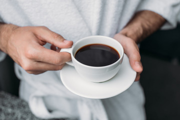 cropped shot of man in bathrobe holding cup of coffee at morning