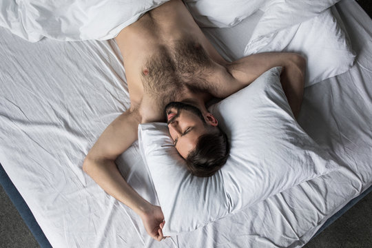 top view of handsome shirtless bearded man sleeping in bed under white blanket