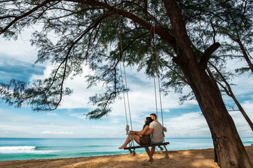 Couple in love on a swing by the sea. Couple in love on an island off the coast. Honeymoon. Couple...