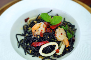Black spaghetti with spicy seafood on white plate.