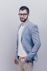 Young successful brunet bearded entrepreneur lawyer in casual smart and fashionable black eyewear is standing on a pre light blue background with hand in pockets and smiling