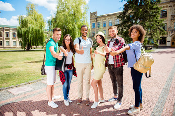 Education is cool! Successful future for smart youth! Six attractive young bachelors are welcoming in their university, standing near the building, gesturing thumbups, smiling, wearing casual smart