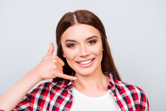 Crlose up portrait of young charming brunette lady, standing on the pure light blue background and smiling, gesturing to call her by her hand, wearing casual checkered shirt