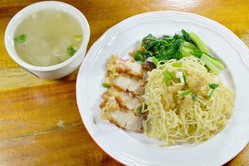 Chinese egg noodles topping crispy pork on plate with soup