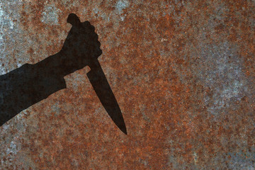 Human hand with killing knife silhouette in shadow on rust wall background. Illustration for criminal news and chronicles.