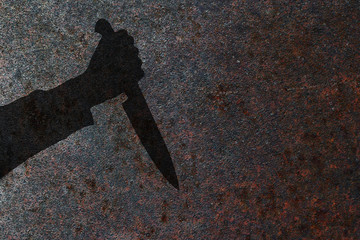 Human hand with killing knife silhouette in shadow on rust wall background. Illustration for criminal news and chronicles.