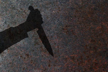 Human hand with killing knife silhouette in shadow on rust wall background. Illustration for...