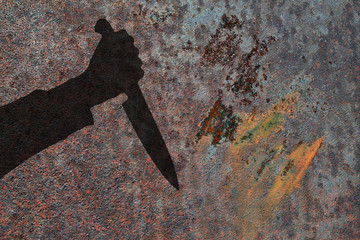 Human hand with big killing knife silhouette in shadow on rust wall background. Illustration for criminal news.