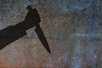 Human hand with killing kitchen knife silhouette in shadow on rust wall background. Illustration for criminal chronicles.