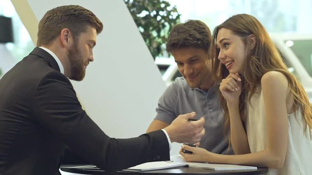 Young pretty couple talking with dealer and getting keys after buying car in office