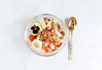 Healthy breakfast with yoghurt, strawberries, bananas, nuts, seeds and pansy flower. Vegan breakfast. Plantbased diet. Marble background.