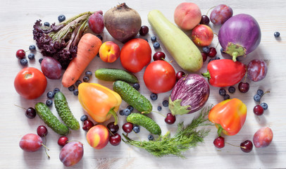 A variety of fresh vegetables, fruits and berries lie on a wooden surface, the top view