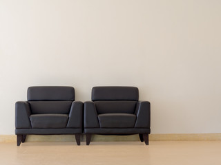 The black sofa is located in the room. There is a white concrete wall.